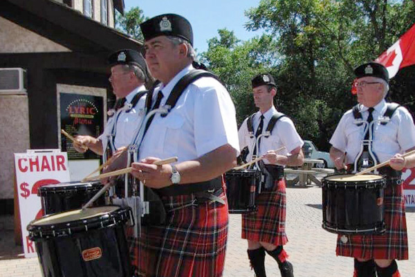 Four drummers in kilts with Canadian flag in background.